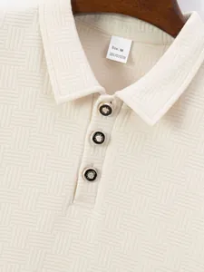 Close-up of cream jacquard polo shirt collar with decorative black and gold buttons