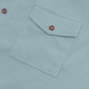 Close-up view of light blue corduroy fabric texture and pocket button on men's shirt.