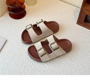 Gros plan de sandales beiges à double bride et boucles en bronze sur fond texturé