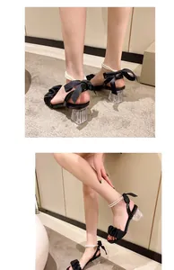 Close-up of black sandals with transparent heels, pearl ankle straps, and satin bow details