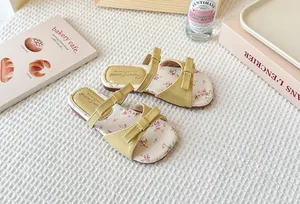 Primer plano de sandalias planas para niñas con estampado floral y un elegante lazo veraniego.