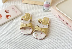 Detalle de sandalias planas para niña con estampado floral, lazos y correas de charol