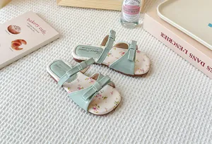 Pantuflas infantiles verde pastel con flores y lazos decorativos en un fondo acogedor