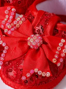 Macro detail of red baby princess shoe with sequined bow and rhinestone accents.