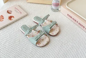 Detalle de sandalias verde menta para niña con estampado floral y elegante lazo decorativo.