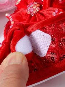 Detailed macro view of red sequin baby princess shoe showing white Velcro fastener strap