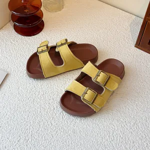 Sandales style Birkenstock en daim jaune à double boucle sur une table texturée blanche