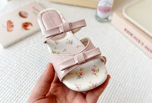 Primer plano de sandalias rosas florales para niña con detalles de lazos y brillo.