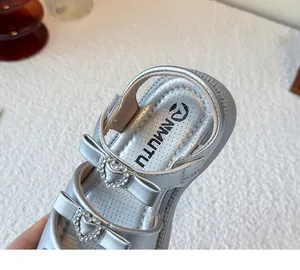 Detalle de sandalias plateadas para niñas con lazos y brillantes detalles de strass de corazón.