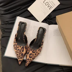 Nahaufnahme von Maultier-Sandalen mit Leopardenmuster auf einem Buch