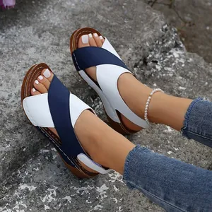 Primer plano de sandalias con cuña de tiras cruzadas en azul y blanco usadas al aire libre.