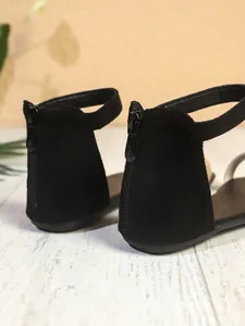 Primo piano del dettaglio della cerniera posteriore sui sandali piatti in camoscio nero.