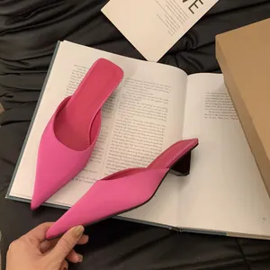 Detailansicht modischer hellrosa Pantoletten mit spitzer Kappe und Blockabsatz auf Buch