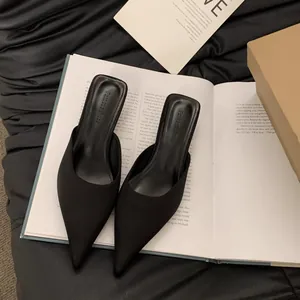 Makroansicht schwarzer spitzer Mules mit strukturiertem Finish und Branding