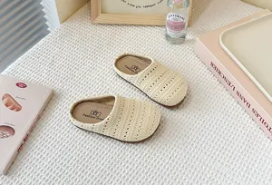 Primer plano de mules para niños de punto calado beige sobre una textura de gofre blanco