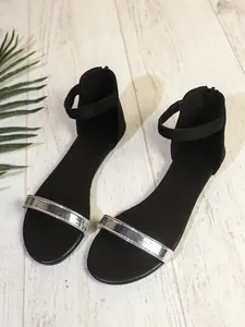 Vista dettagliata di sandali piatti neri minimalisti con cinturino metallico argento e caviglia