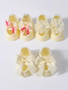 Close-up detail of three pairs of yellow infant socks with lace flowers and decorative bows