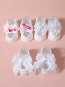 Detailed view of three pairs of white infant socks with bows and flowers on pink background.