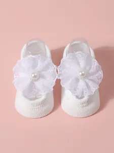 Adorable white knitted baby floor socks with lace flower and pearl detail on pink background