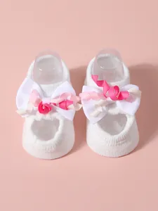Close-up detail of soft white infant socks featuring large pink and white ribbon bows