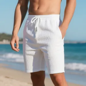 Detail of men's white ribbed beach shorts with drawstring waist in a sunny outdoor setting.