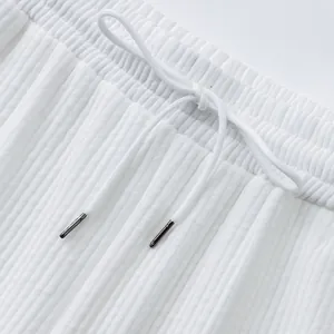 Detail of white jacquard shorts showing elastic waistband and drawstring with metal aglets.