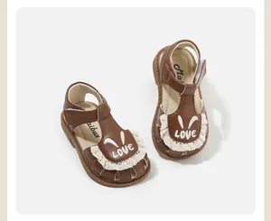 Detalle de sandalias marrones para bebé con encaje blanco y estampado de conejo LOVE.