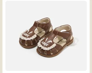 Detalle de sandalias marrones para niña pequeña con encaje y bordado de conejito
