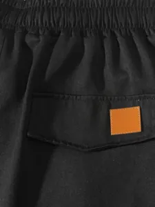 Dettaglio di pantaloncini cargo neri con vita elastica e toppa in pelle marrone scuro