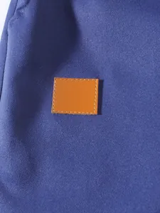 Dettaglio della toppa quadrata arancione cucita sul tessuto blu dei pantaloncini cargo