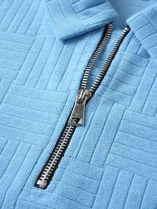 Close-up detail showing the silver metal zipper and unique textured fabric of the blue polo shirt