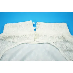 Dettaglio dello scollo di una tuta in pizzo bianco con elegante chiusura a bottoni di perla