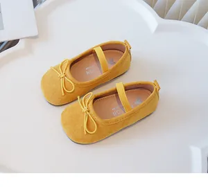 Close-up of yellow girl's flats with bow and elastic strap on a white background