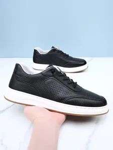 Detailed view of men's black pebbled leather breathable sneakers held by hand