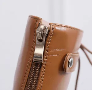 High-quality close-up of smooth brown leather boot detail with gold zipper and snap button.