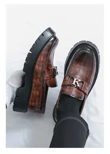 Close-up detail of brown crocodile-textured loafers with a thick sole and metal K buckle