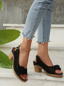 Detailansicht eleganter schwarzer Sandalen mit Blockabsatz, Hohlmuster und Blumenakzent