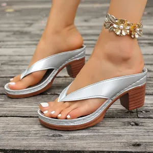 Detailed view of silver metallic thong sandals with brown block heels on wood background