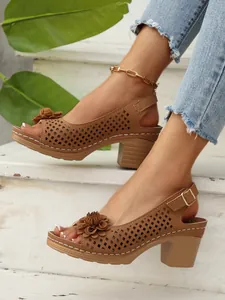 Nahaufnahme von braunen Sandalen mit Blockabsatz, Blumen und Lochmuster-Details.