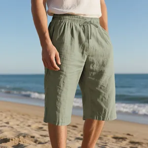 Breathable men's olive green linen shorts with elastic drawstring waist on a sandy beach