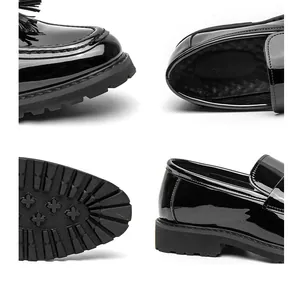 Primer plano de mocasines de charol negro para hombre con borlas y suelas gruesas.