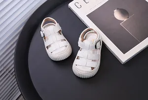 Close-up of white baby closed-toe sandals on a black tray with a magazine