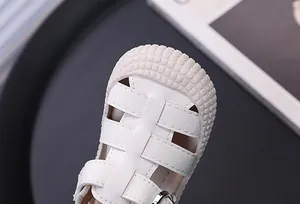 Close-up of white toddler sandal with protective rubber toe cap and woven straps