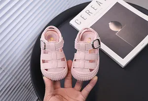 Pink baby sandals with soft soles and buckle detail held by hand