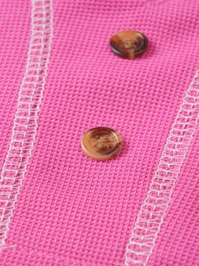 Macro view of pink waffle-knit fabric and brown marbled buttons on Henley shirt.