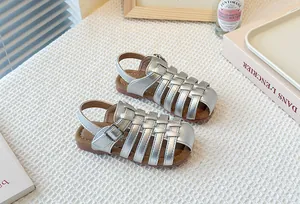 Detailed view of silver metallic woven hollow-out children's Roman sandals on textured mat