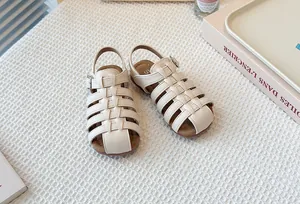 Detailed view of beige woven hollow-out children's Roman sandals on a soft white mat