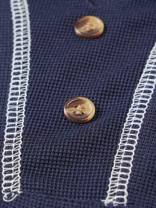 Close-up detail of navy waffle knit Henley shirt with buttons and white stitching.