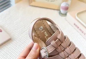 Detailed view of the pink braided faux leather and buckle on kids' Roman sandals