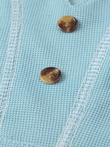 Macro detail of men's blue waffle knit Henley shirt with brown buttons and stitching